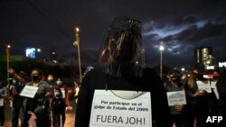 Una mujer vestida de negro con un cartel que decía "Por participar en el golpe de 2009. ¡Fuera JOH!" participa en una protesta en demanda de la renuncia del presidente hondureño Juan Orlando Hernández, en Tegucigalpa el 1 de marzo de 2021.