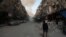 FILE - A Syrian man on crutches walks down a street as smoke billows in the rebel-held town of Douma, in the besieged Eastern Ghouta region on the outskirts of the capital Damascus, following air strikes by regime forces on the area on Feb. 23, 2018.