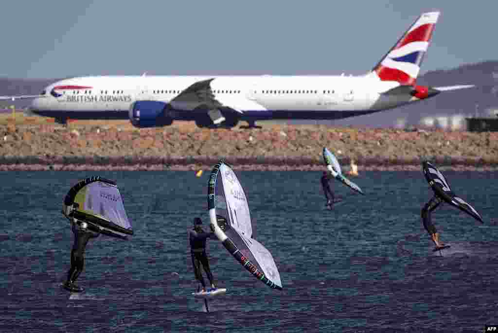 A group of wing surfers ride their boards as a British Airways plane prepares to take-off at Sydney International Airport on a windy spring day, Australia. (Photo by DAVID GRAY / AFP)