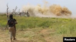 An Islamist rebel fighter walks as smoke rises after what activists said was an airstrike by forces of Syria's President Bashar al-Assad at Qarmeed camp, after Islamist rebel fighters took control of the area, April 27, 2015. 