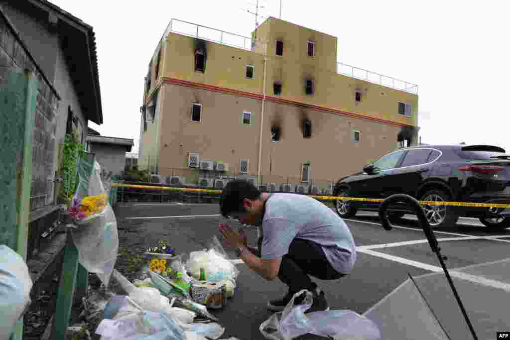 A man prays next to flowers and tributes laid at the scene where 33 people died and scores were injured in a suspected arson attack on an animation company building in Kyoto, Japan.