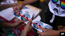 Pendukung memotong stiker pemilu yang mempromosikan mantan Presiden Brasil Luiz Inacio Lula da Silva, yang mencalonkan diri sebagai presiden lagi, di Sao Paulo, Brasil, Kamis, 27 Oktober 2022. (Foto: AP)