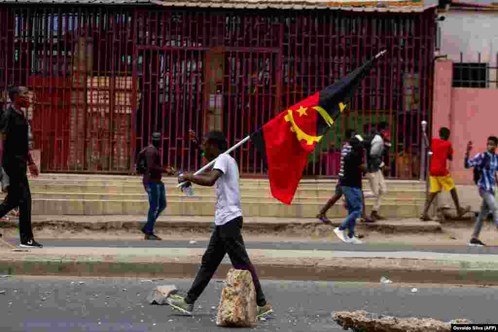 Um manifestante carrega a bandeira angolana enquanto caminha por uma rua durante a manifesta&#231;&#227;o anti-governo em Luanda. A pol&#237;cia anti-motim, alguns montados em cavalos, disparou g&#225;s lacrimog&#233;neo e agrediu dezenas de manifestantes que tomaram as ruas da c