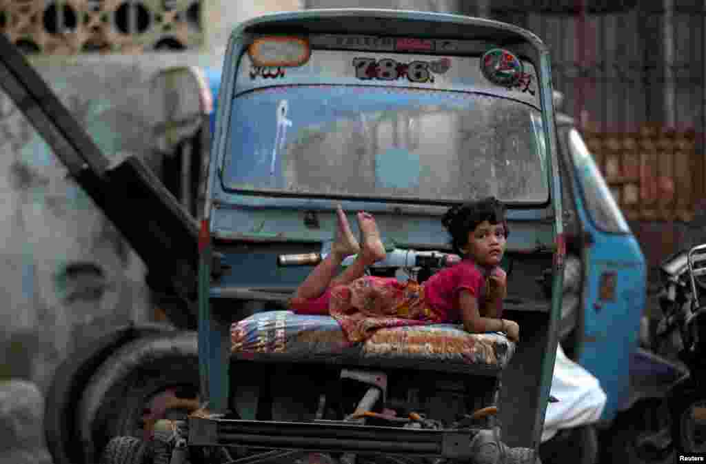 A girl rests on a rickshaw parked along a street in Karachi, Pakistan.