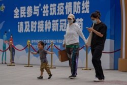 FILE - People walk by a billboard reading 'All people participate in building a line of defense against the epidemic, please get the vaccine in time' in Beijing, May 24, 2021.