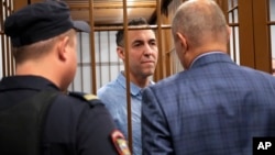 French citizen Laurent Vinatier, center, stands in a defendant's cage speaking with his lawyer as a court convicted him of collecting military information, at the Zamoskvoretsky District Court in Moscow, Russia, Oct. 14, 2024.