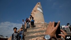 FILE - Locals take snapshots with their cell phones at the historic Dharahara Tower, a city landmark, that was damaged in Saturday’s earthquake in Kathmandu, Nepal, April 27, 2015. 