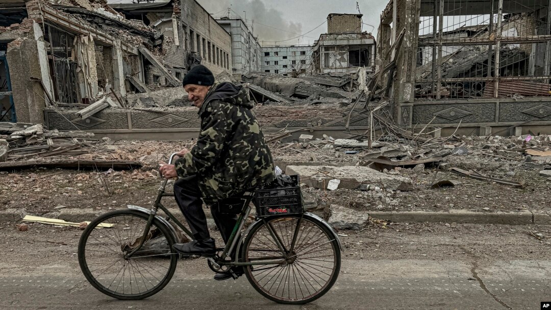 Seorang pria mengendarai sepeda di depan kantor pos yang hancur akibat serangan udara Rusia di Kurakhove, wilayah Donetsk, Ukraina, pada 7 November 2024. (Foto AP/Anton Shtuka)