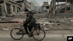 Seorang pria mengendarai sepeda di depan kantor pos yang hancur akibat serangan udara Rusia di Kurakhove, wilayah Donetsk, Ukraina, pada 7 November 2024. (Foto AP/Anton Shtuka)