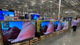 FILE - A shopper passes by a line of large-screen televisions on display in a Costco warehouse, Feb. 3, 2025, in east Denver. Flat screen TVs are the ancestor of the first televisions developed by Farnsworth. (AP Photo/David Zalubowski)