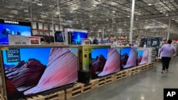 FILE - A shopper passes by a line of large-screen televisions on display in a Costco warehouse, Feb. 3, 2025, in east Denver. Flat screen TVs are the ancestor of the first televisions developed by Farnsworth. (AP Photo/David Zalubowski)