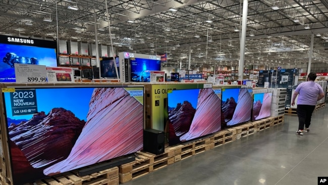 FILE - A shopper passes by a line of large-screen televisions on display in a Costco warehouse, Feb. 3, 2025, in east Denver. Flat screen TVs are the ancestor of the first televisions developed by Farnsworth. (AP Photo/David Zalubowski)