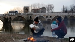 Migrants hold their babies as they try to warm themselves next to a river in Edirne, Turkey, near Turkish-Greek border, March 4, 2020.