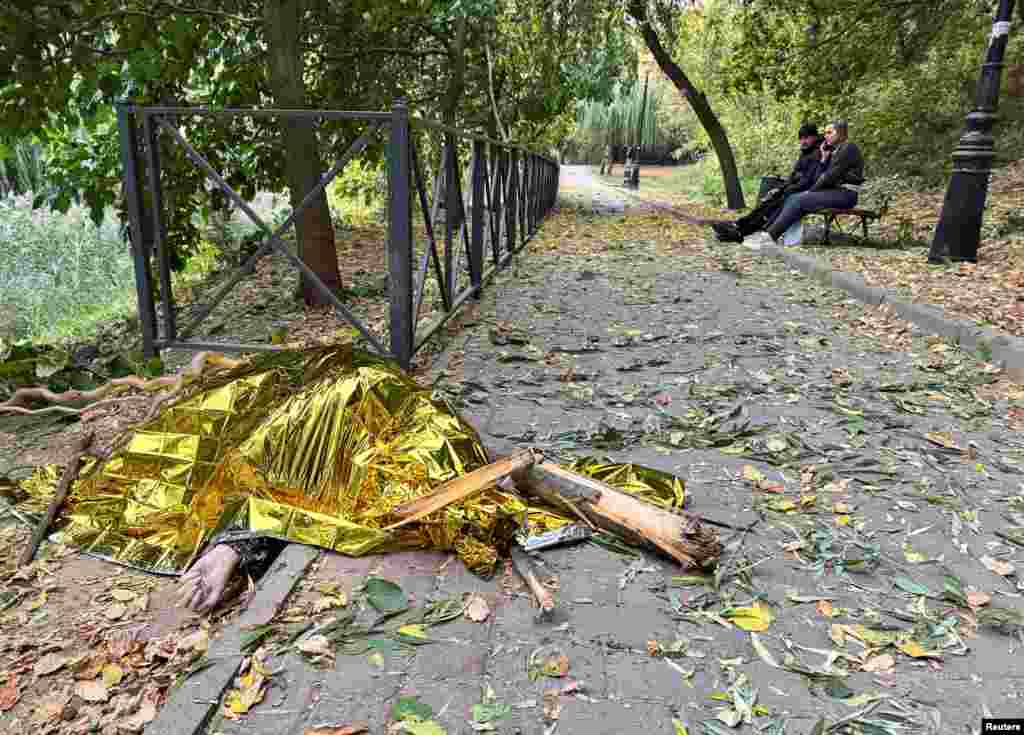 Locals sit on a bench at a lake shore as the body of a woman killed during a Russian air strike lies nearby in Kharkiv, Ukraine.