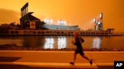 FILE - In this Wednesday, Sept. 9, 2020 file photo, a jogger runs along McCovey Cove outside Oracle Park in San Francisco, under darkened skies from wildfire smoke. Worsening climate change requires that the United States do much more to track and manage 