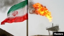 FILE PHOTO: A gas flare on an oil production platform is seen alongside an Iranian flag in the Gulf, July 25, 2005. 