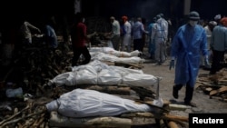 A health worker wearing personal protective equipment (PPE) walks past the funeral pyres of those who died from the COVID-19 during a mass cremation at a crematorium in New Delhi, India, April 26, 2021.