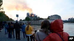 Para pengunjung menyaksikan dari kejauhan saat api dan asap membubung dari Katedral Notre Dame yang terbakar di Paris, Senin, 15 April 2019. 