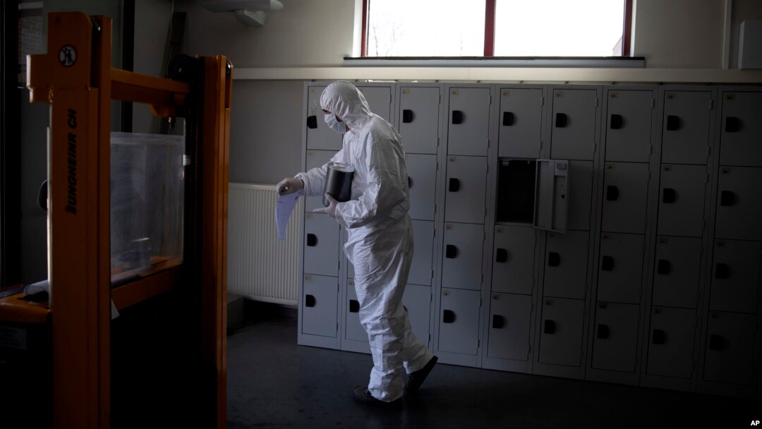 Seorang pekerja mengenakan baju pelindung membawa bejana berisi abu pasien Covid-19 di krematorium Pontes di Wilrijk, dekat Antwerp, Belgia, 3 April 2020.