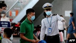 Staf Pusat Pengendalian Penyakit Vietnam (kanan) membantu para penumpang saat antre pemeriksaan suhu di terminal keberangkatan bandara internasional Danang, 27 Juli 2020. (Foto oleh Hoang Khanh / AFP)