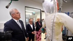 Perdana Menteri Australia Scott Morrison (kiri) mengamati APD dalam tur di Peter Doherty (Institute for Infection and Immunity) di Melbourne, Selasa, 14 Desember 2021. (Andrew Henshaw/AAP Image via AP)