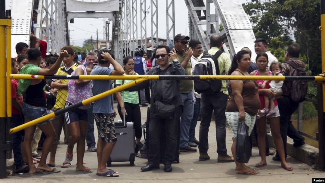 FILE - People stand next to a closed gate as they wait to try to cross La Union international bridge, on the border with Colombia at Boca de Grita in Tachira state, Venezuela, Aug. 29, 2015. 