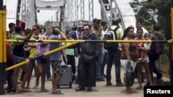 FILE - People stand next to a closed gate as they wait to try to cross La Union international bridge, on the border with Colombia at Boca de Grita in Tachira state, Venezuela, Aug. 29, 2015. 