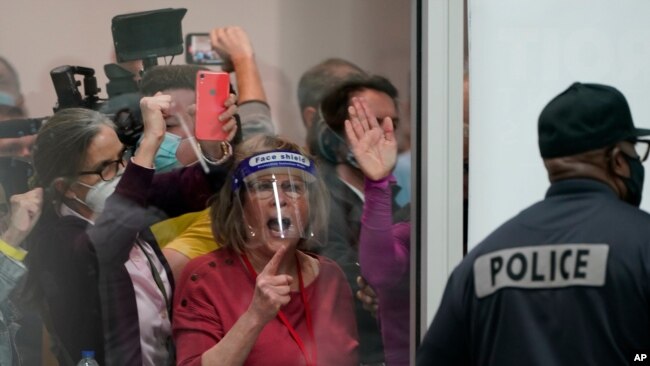 FILE - In this Nov. 4, 2020, photo, election challengers in Detroit yell as they look through the windows of the central counting board as police were helping to keep additional challengers from entering due to overcrowding.