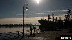 La gente habla con sus teléfonos inteligentes en una orilla del río Dnipro después de la retirada de Rusia de Kherson, en Jersón, Ucrania, 14 de noviembre de 2022. REUTERS/Valentyn Ogirenko