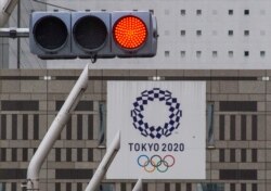 FILE - A red traffic light is seen on a street near the Tokyo Metropolitan Government Building displaying a banner of the Tokyo 2020 Olympics Games, in Tokyo, Japan, May 31, 2021.