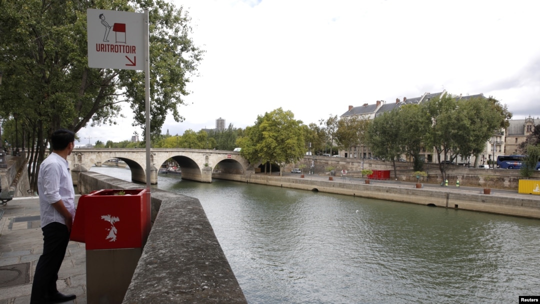 A journalist poses in front of a bright red, eco-friendly urinal on the Ile Saint-Louis along the Seine River in Paris, France, Aug. 13, 2018. 