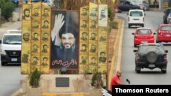 Un hombre en una motocicleta posa junto a un anuncio que representa al líder de Hezbolá en el Líbano, Sayyed Hassan Nasrallah.