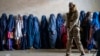 FILE - A Taliban fighter stands guard as women wait to receive food rations distributed by a humanitarian aid group, in Kabul, Afghanistan, May 23, 2023. 