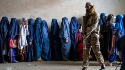 FILE - A Taliban fighter stands guard as women wait to receive food rations distributed by a humanitarian aid group, in Kabul, Afghanistan, May 23, 2023. 