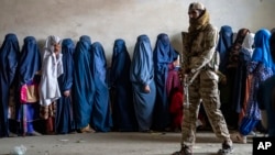 FILE - A Taliban fighter stands guard as women wait to receive food rations distributed by a humanitarian aid group, in Kabul, Afghanistan, on May 23, 2023. 