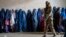 FILE - A Taliban fighter stands guard as women wait to receive food rations distributed by a humanitarian aid group, in Kabul, Afghanistan, on May 23, 2023. 