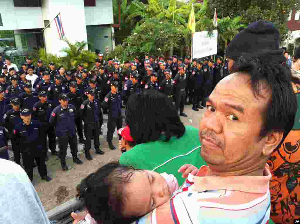 Man with baby watches Thai police and soldiers line up in front of disputed flood gate at Samwan canal, Bangkok, October 31, 2011. (VOA)