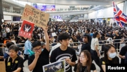 FILE - Anti-extradition bill protesters hold up placards for arriving travelers during a protest at the arrival hall of Hong Kong International Airport in Hong Kong, China, Aug. 9, 2019. 