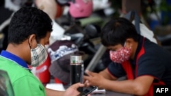 FILE - Men wear face masks as a preventive measure against the COVID-19 novel coronavirus as they use their mobile phones in Phnom Penh on March 18, 2020.