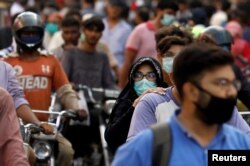 FILE - A woman wearing a face mask rides as a passenger on a motorbike amid a rush of people outside a market, amid the coronavirus pandemic, in Karachi, Pakistan, June 8, 2020.