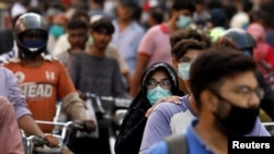 FILE - A woman wearing a face mask rides as a passenger on a motorbike amid a rush of people outside a market, amid the coronavirus pandemic, in Karachi, Pakistan, June 8, 2020.