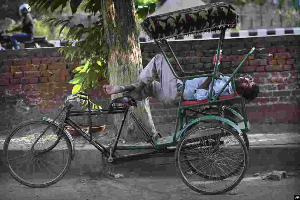 Seorang pengemudi rickshaw, semacam becak di India, tidur di rickshawnya pada suatu siang yang terik di New Delhi, India.