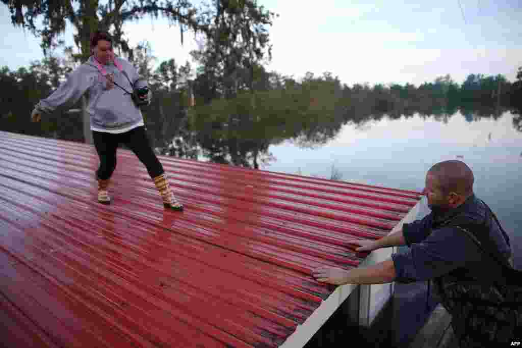 Wendy Lawshe (L) walks along the roof of her father&#39;s house as her husband waits for her in a boat as they retrieve pictures from the walls of the home that is flooded in in Andrews, South Carolina.&nbsp; The state has experienced record rainfall amounts causing severe flooding and officials expect the damage from the flooding waters to be in the billions of dollars.