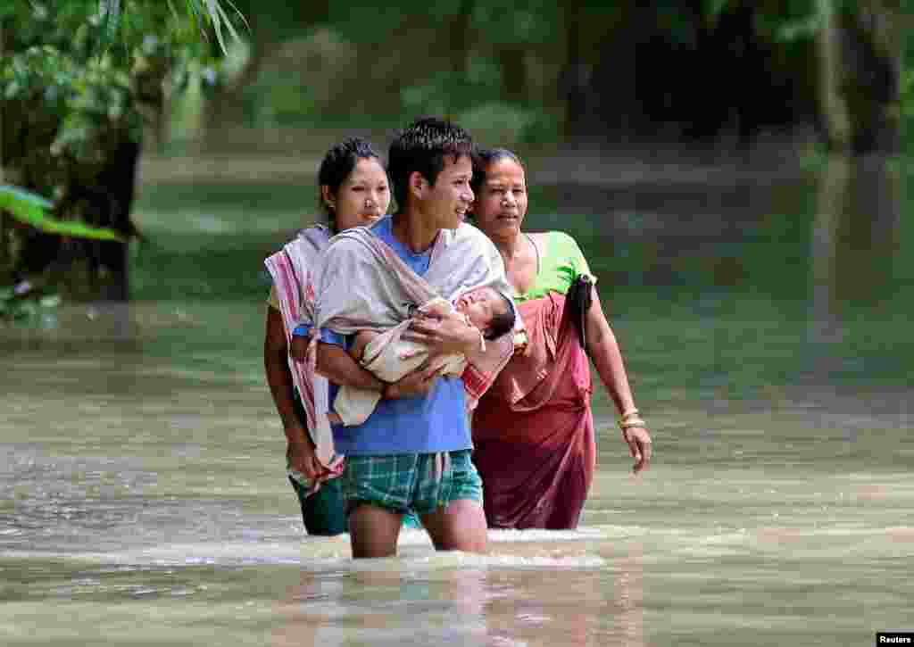 A man carries his new born baby as he and his family members wade through a flooded area to reach a relief camp at a village in Barpeta district of the northeastern state of Assam, India.