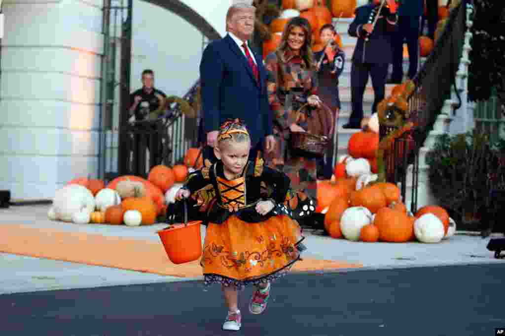 President Donald Trump and first lady Melania Trump watch a young girl as they give candy to children during a Halloween trick-or-treat event on the South Lawn of the White House, Oct. 28, 2019, in Washington.