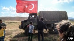 FILE - A man waves a Turkish national flag as a Turkish army vehicle drives past during a demonstration in support of the Turkish army's operation near the Turkey-Syria border near Reyhanli, Hatay, Oct. 10, 2017.