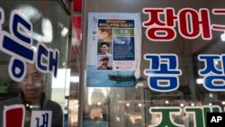 FILE - Restaurant owner Shin Byung-chul looks from behind a flyer he put up of Kenneth Barthel, who was abandoned in the area as a child and later adopted to Hawaii at 6 years old, at his restaurant in Busan, South Korea, May 17, 2024.