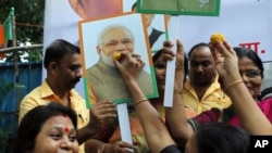 A supporter of India's ruling Bhartiya Janata Party (BJP) feeds sweets to a portrait of Prime Minister Narendra Modi as she celebrates with others the revocation of Kashmir's special constitutional status, in Mumbai, Aug. 6, 2019. 