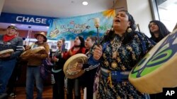 FILE - Roxanne White, right, a member of the Yakama Nation, sings during a protest inside a Chase bank branch, May 8, 2017, in Seattle. Climate activists opposed to oil pipeline projects have called on several financial institutions not to help build pipelines.