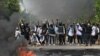 Anti-coup protesters flash the three-finger salute, a symbol of resistance, as they are confronted by security forces in Thaketa township, Yangon, Myanmar, March 27, 2021. 